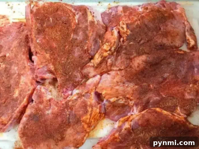 Raw, seasoned pieces of meat are spread out on a white surface, showcasing a reddish hue from spices sprinkled on top, reminiscent of the best baked pork chops ready for the oven.