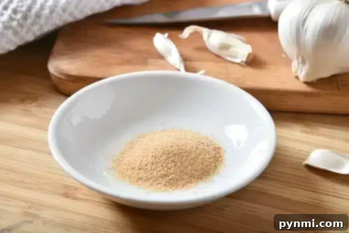 A small white dish containing garlic powder rests on a wooden surface, perfect for seasoning the best baked pork chops. Behind it, garlic cloves and a cutting board with a knife add to the culinary tableau.