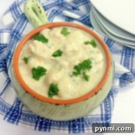 A ceramic bowl filled with creamy Instant Pot gnocchi soup garnished with parsley sits on a blue and white checkered cloth. A stack of white plates rests in the background.