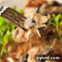 Close-up of a fork holding tender chicken marsala in creamy mushroom sauce, with greens blurred in the background.
