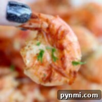 Close-up of a hand with glittery black nails holding a perfectly cooked shrimp, garnished with herbs, straight from the air fryer.