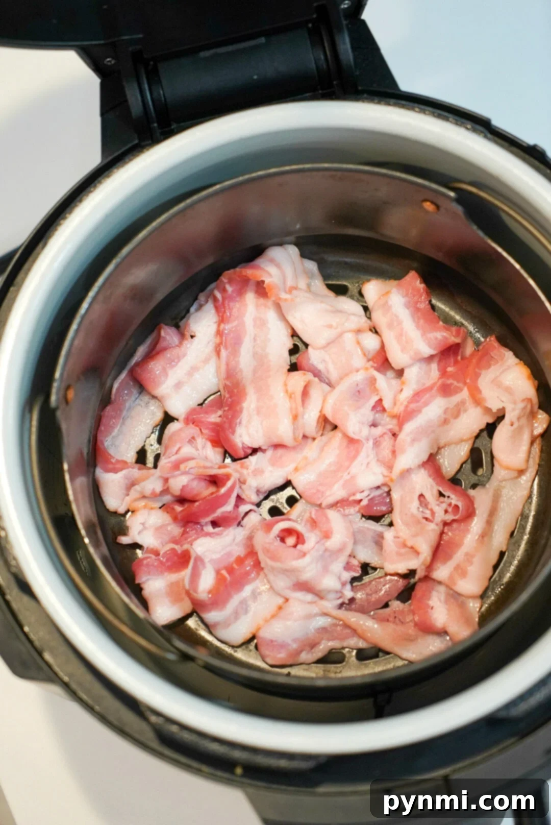 Crispy bacon cooking in a Ninja Foodi air fryer basket, showing the strips perfectly spaced for even cooking and optimal crispness.