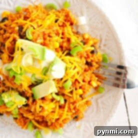 A plate of vibrant instant pot enchilada rice topped with cheese, avocado, and chopped green onions sits invitingly, with a fork ready on the side.