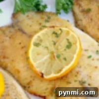Frozen fish in an air fryer, no breading, are elegantly garnished with a lemon slice and parsley on a white plate.