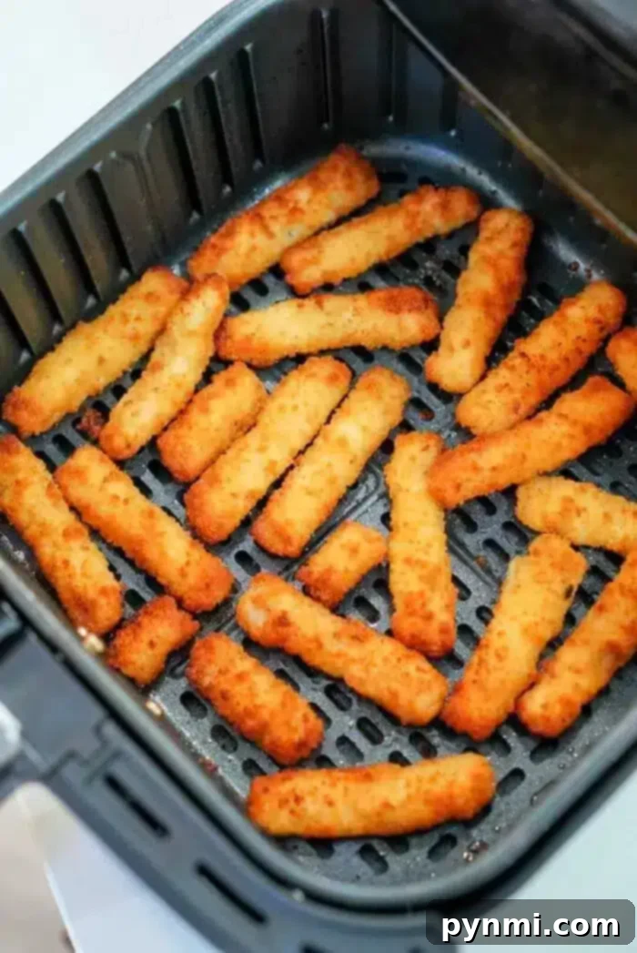 Several perfectly golden brown and evenly cooked air fryer fish sticks arranged in a single layer inside an open air fryer basket with a perforated bottom.