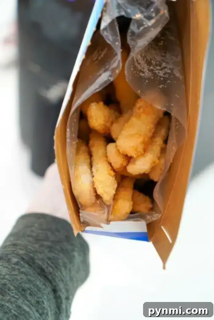 An open cardboard box revealing frozen fish sticks, partially wrapped in clear plastic, ready for air frying.