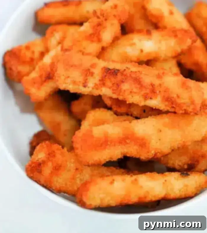 A white bowl brimming with numerous crispy, golden-brown air fryer fish sticks, artfully arranged for serving.