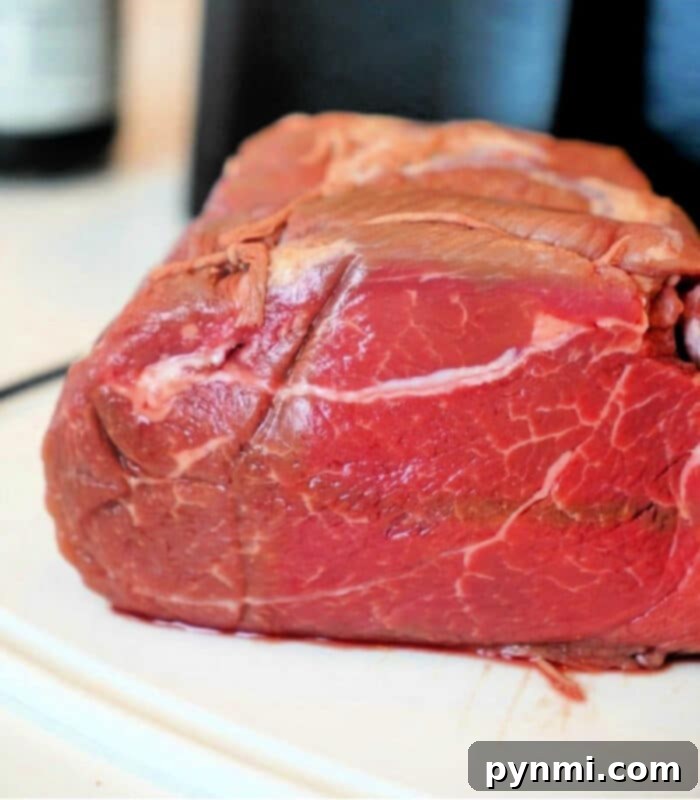 A raw beef roast, beautifully marbled, resting on a clean white surface, ready to be transformed in the air fryer. The rich red color of the meat contrasts with a softly blurred background.