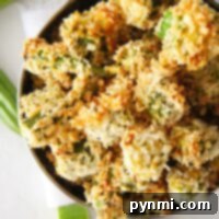 A bowl of crispy, air fryer okra pieces on a white surface, with some fresh okra in the background.