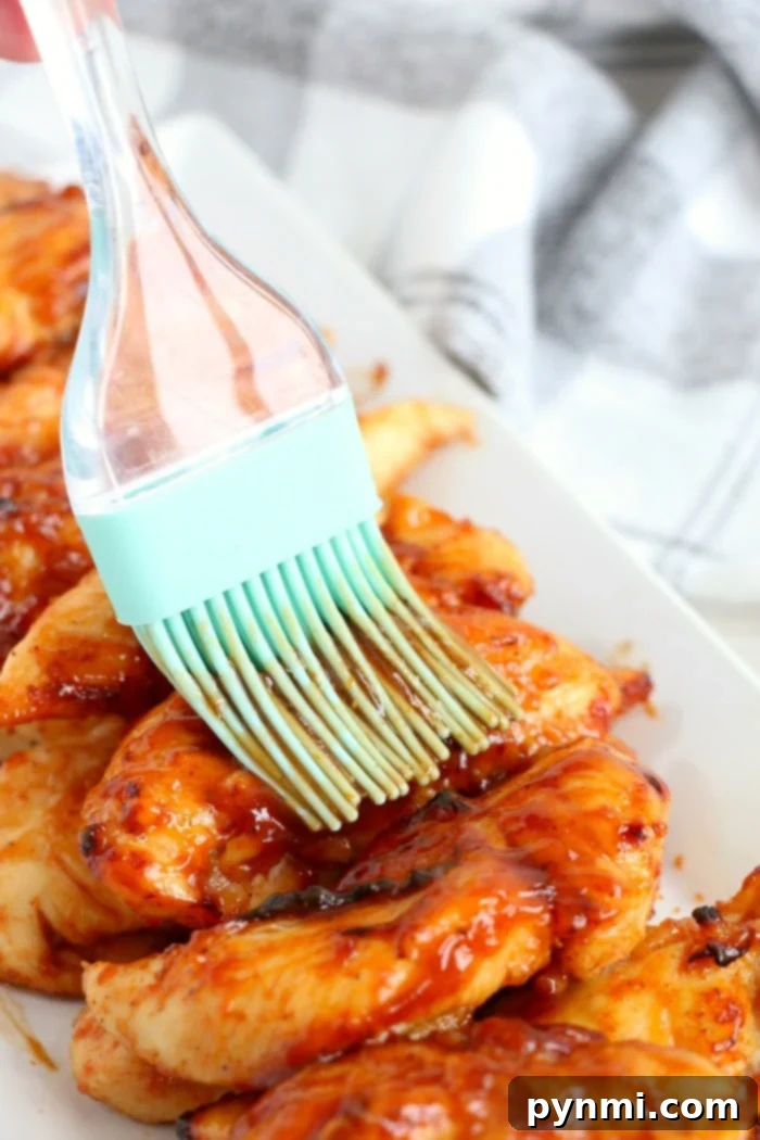 A cooking brush applies a final layer of barbecue sauce to freshly air-fried chicken tenders on a white plate, highlighting a delicious no-breading meal.