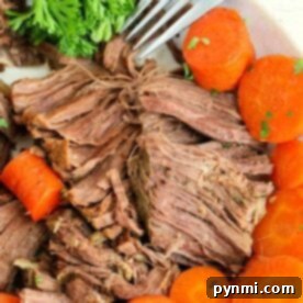 Close-up of a plate with shredded cooked beef, perfectly tender from being a frozen roast in the Instant Pot, surrounded by sliced, cooked carrots and a sprig of fresh parsley. A fork is placed beside the beef, ready to serve.
