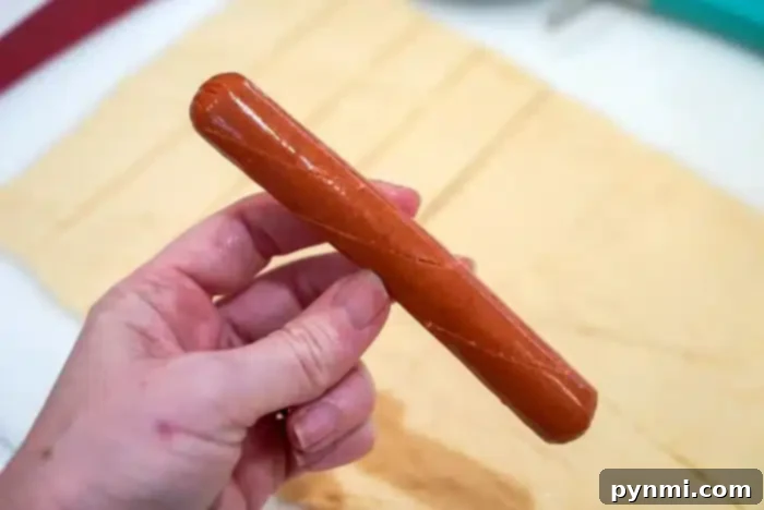 Golden Air Fryer Pigs in Pastry 4 A hand holds a raw hot dog ready to wrap in crescent dough ready to wrap and bake.