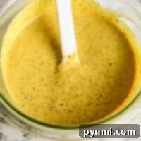 A bowl of creamy mustard pretzel dip sits invitingly, accompanied by a white spatula on a sleek marble surface.