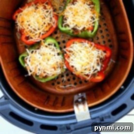 Four halved bell peppers filled with ground meat and shredded cheese make delicious air fryer stuffed peppers, arranged perfectly in the air fryer basket.
