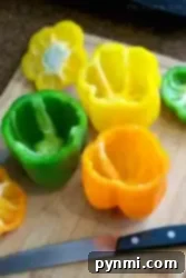 Perfect Air Fryer Stuffed Peppers 8 A wooden cutting board displays hollowed-out bell peppers in vibrant yellow, green, and orange hues. A sharp knife with a black handle lies beside them, perfect for prepping ingredients in your kitchen adventures, whether slicing or learning how to blanch bell peppers.