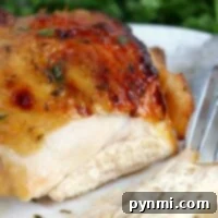 Close-up of marinated chicken breast, perfectly roasted in an air fryer, sliced on a white plate with a fork; herbs in the background.