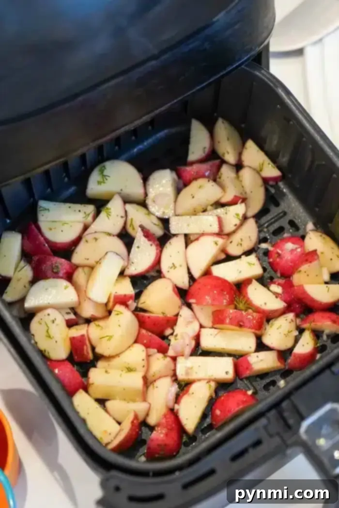 Chopped air fryer red potatoes seasoned with herbs are placed in the basket, ready for cooking.