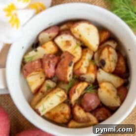A white bowl filled with air fryer red potatoes, garnished with herbs, surrounded by whole red potatoes.