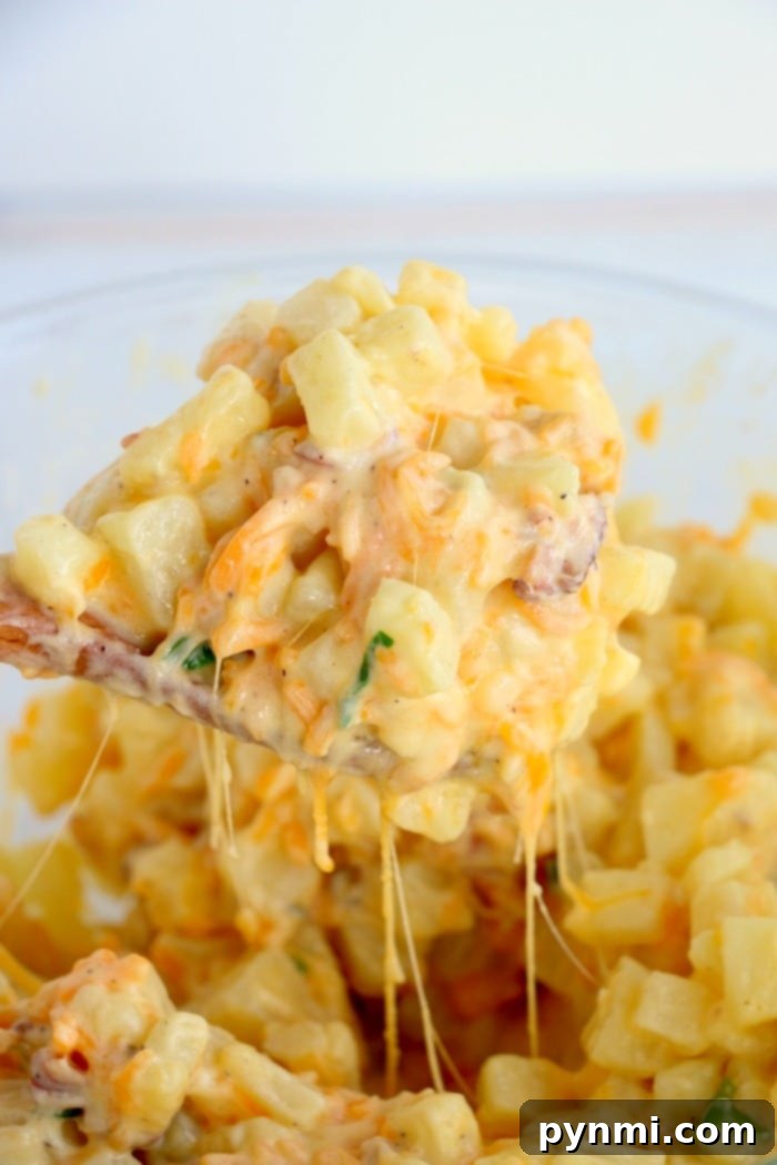 Close-up of cheesy potato casserole recipe with bacon pieces and herbs in a spoonful, showcasing strands of melted cheese and creamy texture.