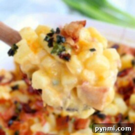 A spoonful of creamy cheesy potato casserole, topped with crispy bacon and herbs.