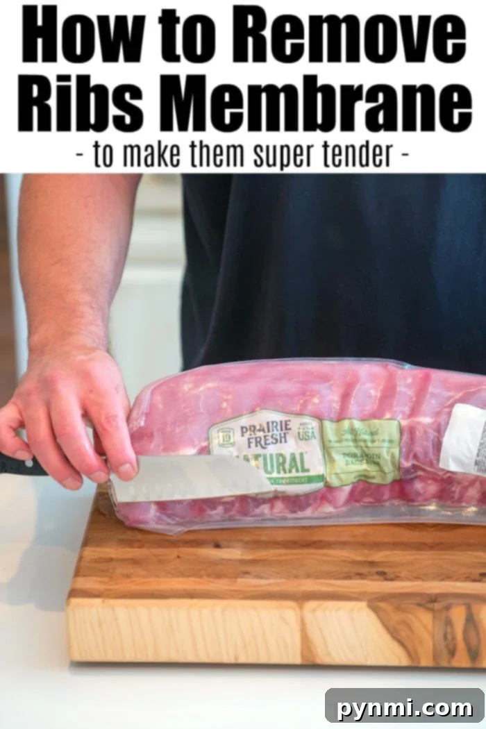 How to remove membrane from ribs so they're super tender. Close-up of a hand carefully removing the thin membrane from the back of a rack of pork ribs on a cutting board, preparing them for maximum tenderness.