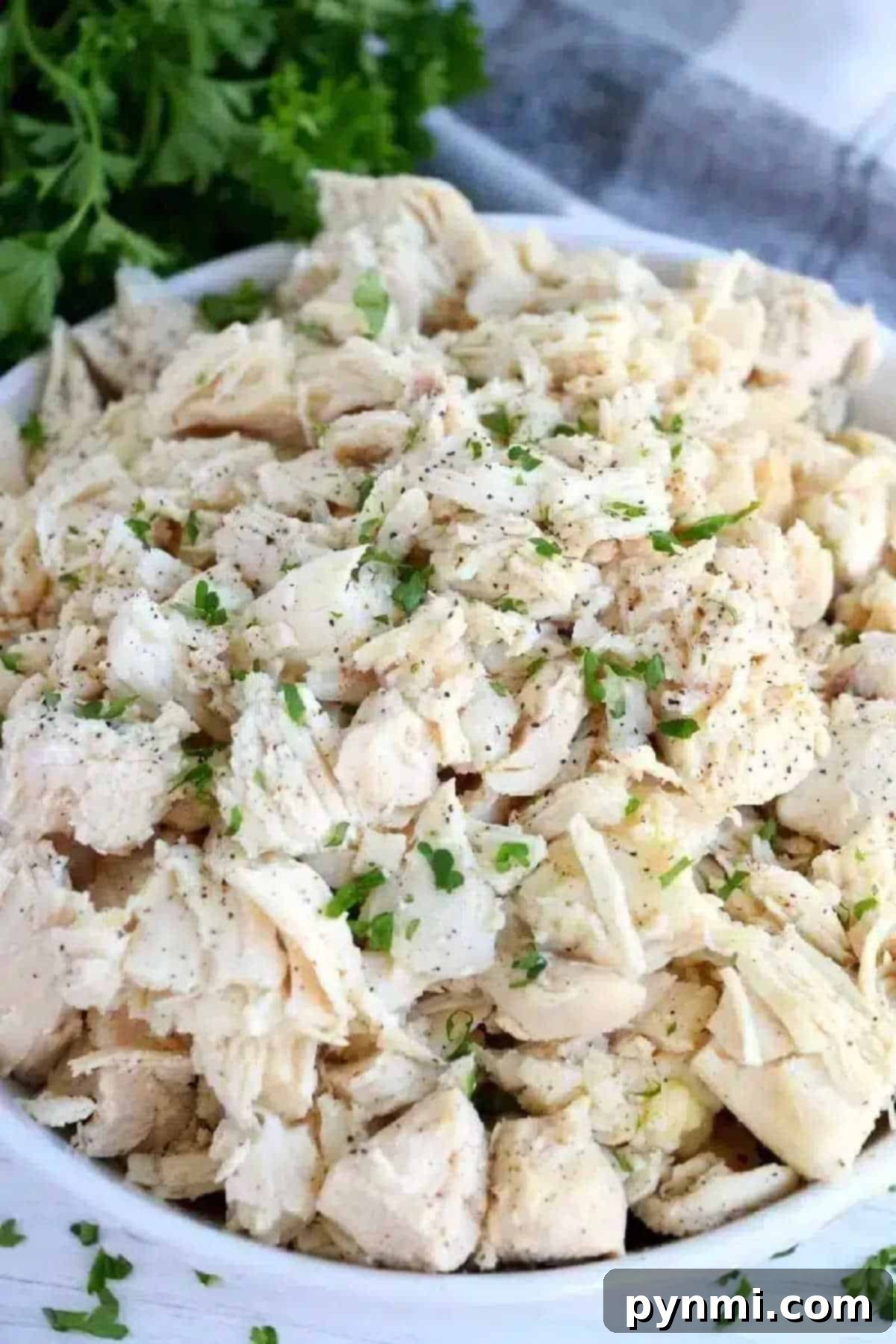 A bowl of perfectly shredded, cooked chicken, lightly seasoned with chopped parsley and black pepper, ready for meal prep or immediate use.