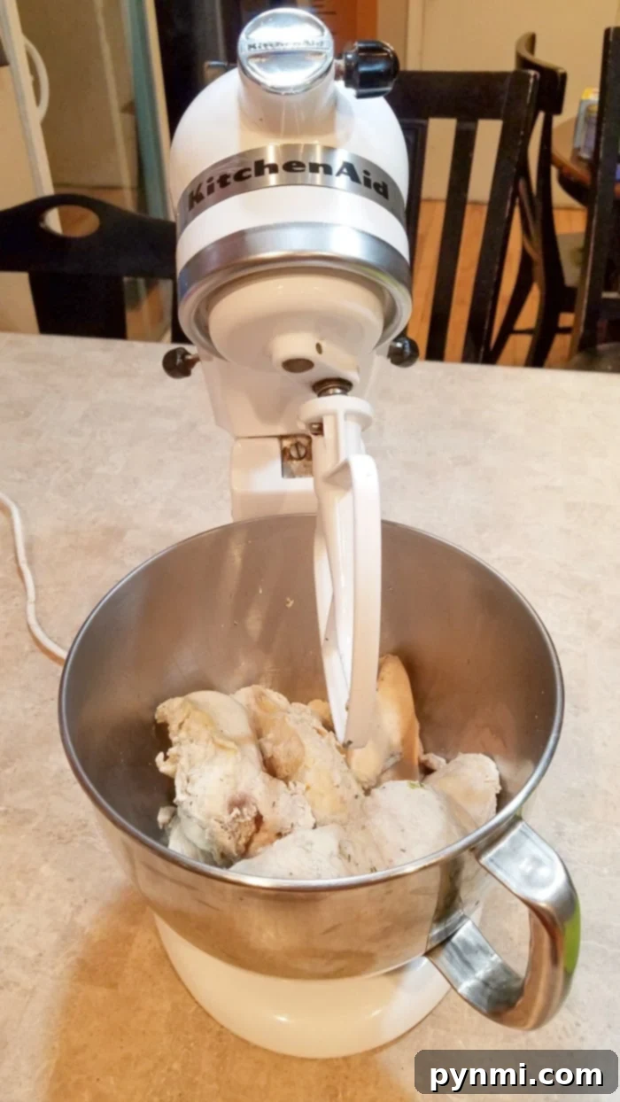 Overhead view of a cooked chicken breast being pulled apart with two forks, demonstrating the ease of shredding.