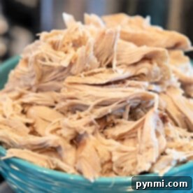 Tender shredded cooked chicken piled high in a blue bowl, garnished with fresh herbs.