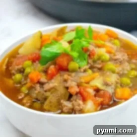 A bowl of Instant Pot beef stew with potatoes, peas, and carrots is topped with fresh parsley, reminiscent of a hearty hamburger soup.