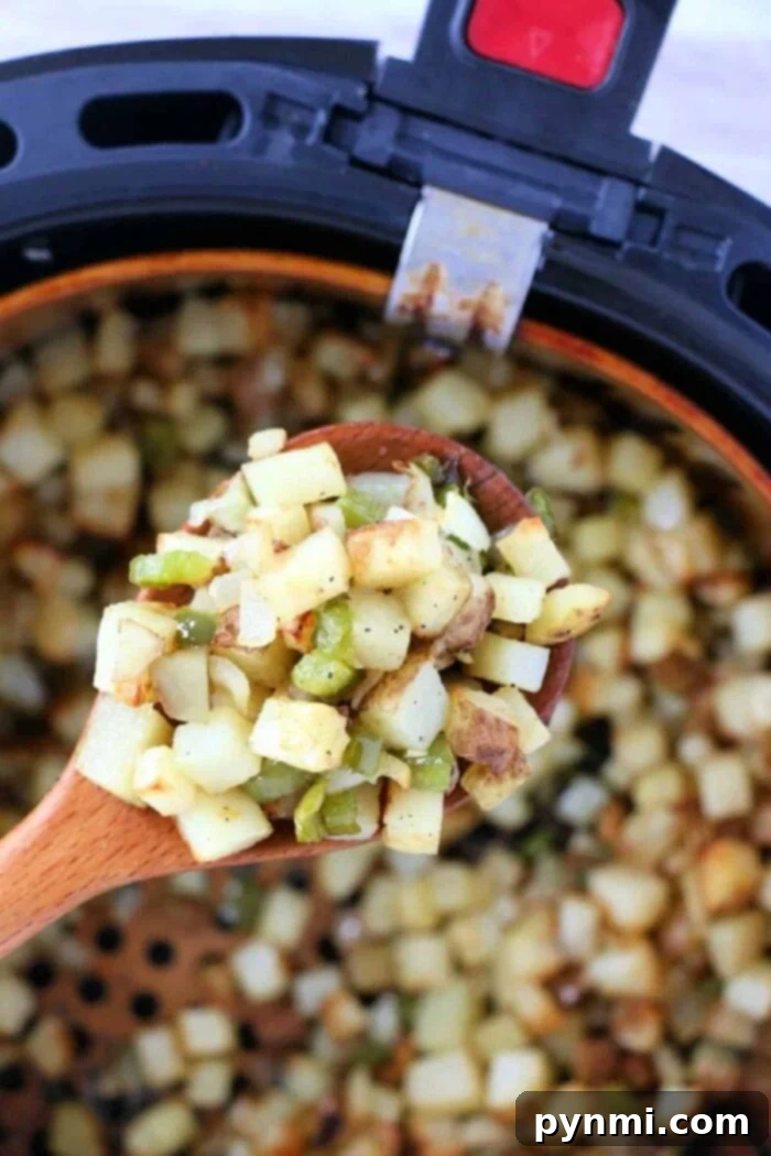 Golden Air Fryer Breakfast Bites 2 A wooden spoon holds diced potatoes and vegetables over an air fryer basket filled with air fryer breakfast potatoes, ready to be served.