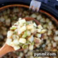 A wooden spoon holds perfectly cooked air fryer breakfast potatoes mixed with vibrant green peppers above the basket, showcasing their crisp texture.