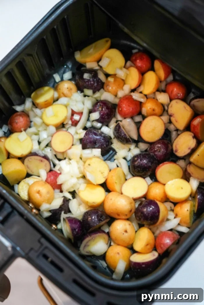 Roasted potatoes in an air fryer, mixed with vibrant chopped onions, are perfectly arranged in the basket and ready for cooking.