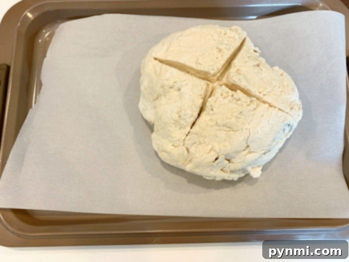 Close-up of the no yeast bread dough on a cutting board, shaped into a ball and scored with an X.
