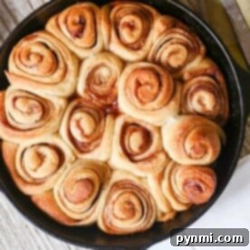 A skillet brimming with freshly baked, golden-brown cinnamon rolls—crafted with a no-yeast recipe—rests on a rustic wooden surface.