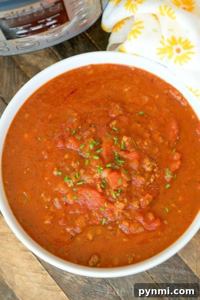 Cook Once, Eat All Week 5 A white bowl filled with chunky tomato and meat stew, perfect for batch cooking, is garnished with chopped herbs and placed on a wooden table. A yellow and white patterned cloth and a pressure cooker are partially visible in the background.
