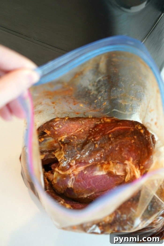 Cook Once, Eat All Week 8 A hand holds an open plastic bag containing raw meat marinated in a red sauce with visible garlic pieces, ready for the air fryer, on a light-colored surface.