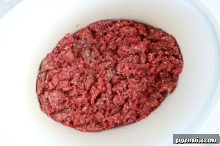 Effortless Crockpot Ground Beef Meals 4 Raw ground beef spread evenly in a white slow cooker, ready for cooking.
