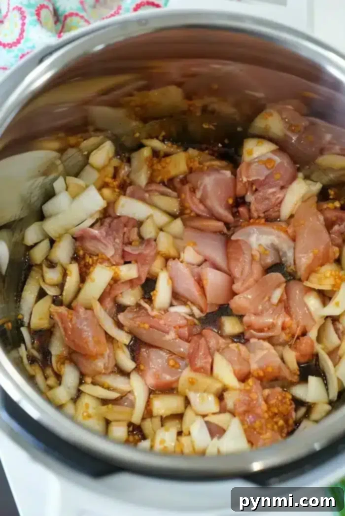 Sticky Sweet Instant Pot Korean Chicken 5 A metal pot contains uncooked diced chicken, chopped onions, and minced garlic. The ingredients are in the process of being sautéed, with some onions already starting to turn translucent, creating the base for a delicious Instant Pot Korean chicken dish.