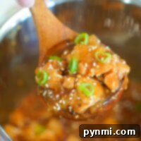 Sticky Sweet Instant Pot Korean Chicken 7 A wooden spoon holding delicious Korean chicken, topped with green onions and sesame seeds, hovers above an Instant Pot.