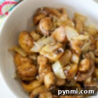 A bowl of air fryer mushrooms with onions, topped with spices, sits next to a colorful patterned towel.