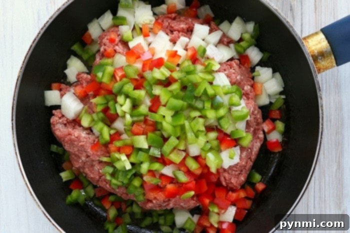 Golden Crispy Air Fryer Empanadas 5 Ground meat with chopped onions, red and green bell peppers sizzles in a black frying pan, perfect for stuffing into air fryer empanadas, illustrating the vibrant filling preparation.