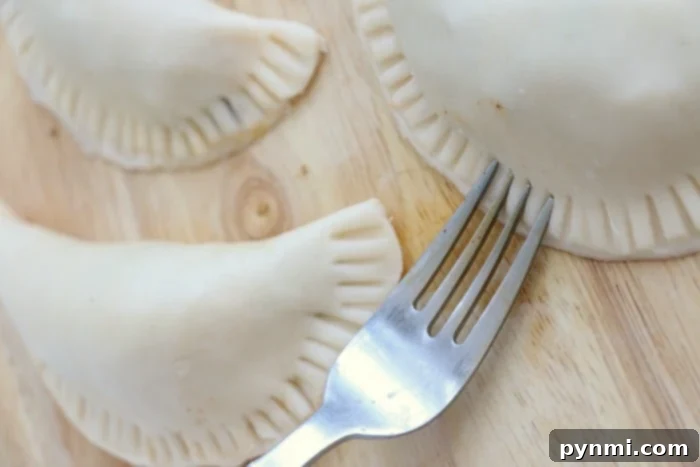 Golden Crispy Air Fryer Empanadas 6 Three uncooked air fryer empanadas rest on a wooden surface, with one showing the delicate marks of a fork pressing its edges, ready for air frying.