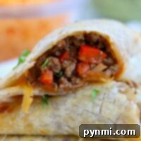 A close-up of two air fryer empanadas, one cut open to reveal a filling of ground meat and chopped red peppers, garnished with herbs, showcasing the delicious interior.