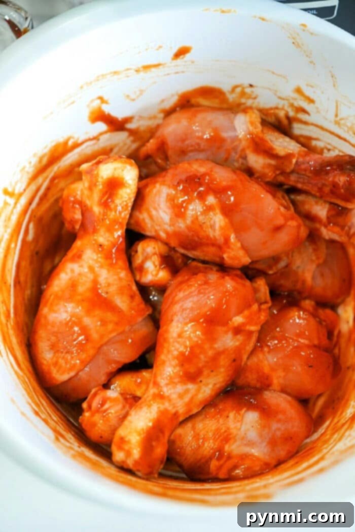 Raw chicken drumsticks coated in a red marinade sit enticingly inside a white bowl, ready to be transformed into a delicious meal with the Ninja Foodi.