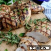 Zesty Lemon Pepper Chicken Marinade 7 Grilled chicken breasts with herbs on a wooden board, infused with a zesty lemon pepper chicken marinade, garnished with parsley, and served alongside a creamy sauce.