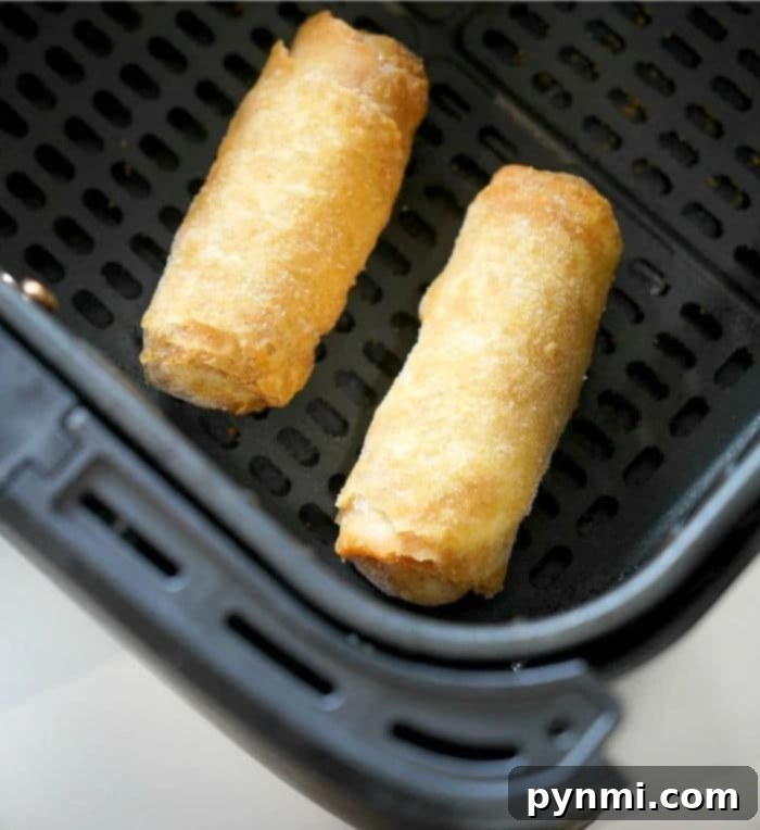Crispy Air Fryer Frozen Egg Rolls 2 Two frozen egg rolls rest in an air fryer basket, their crispy shells hinting at the convenience of preparing frozen egg rolls in an air fryer.