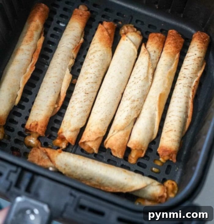 An air fryer basket filled with golden-brown, crispy frozen taquitos, arranged neatly with some cheese oozing from the ends. Perfect for a quick snack or meal.