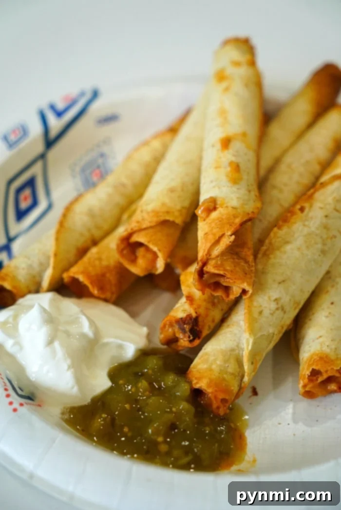 A plate of perfectly cooked chicken taquitos, golden and crispy from the air fryer, garnished with fresh cilantro and a side of dipping sauce.