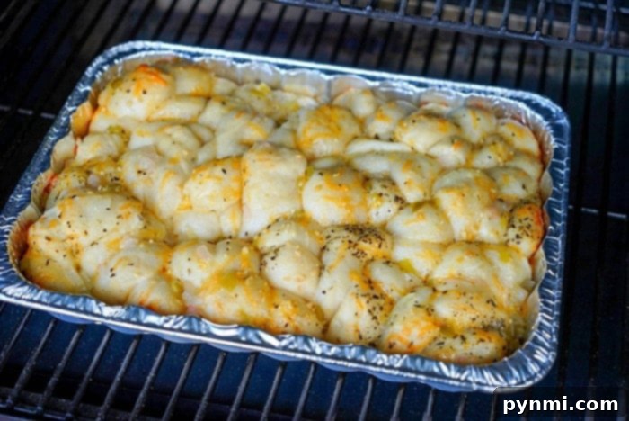 Partially baked smoked bread in a foil pan, covered in cheese, before browning.