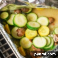 Smoked vegetables take center stage as grilled zucchini and mushrooms are nestled in a foil tray, partially covered with aluminum foil.